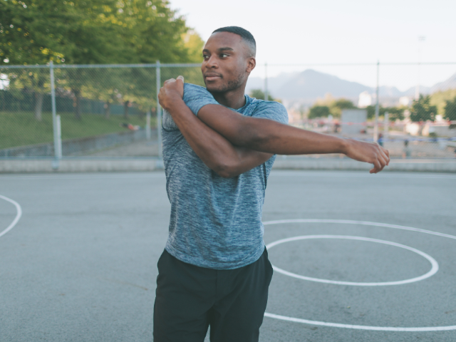  A man stretching his arms outdoors on a basketball court, preparing for a workout.