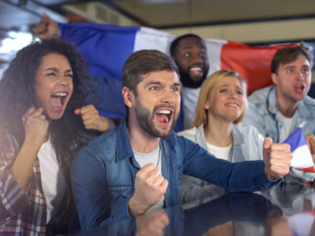 A group of diverse rugby fans cheering while watching a match, with a flag in the background.