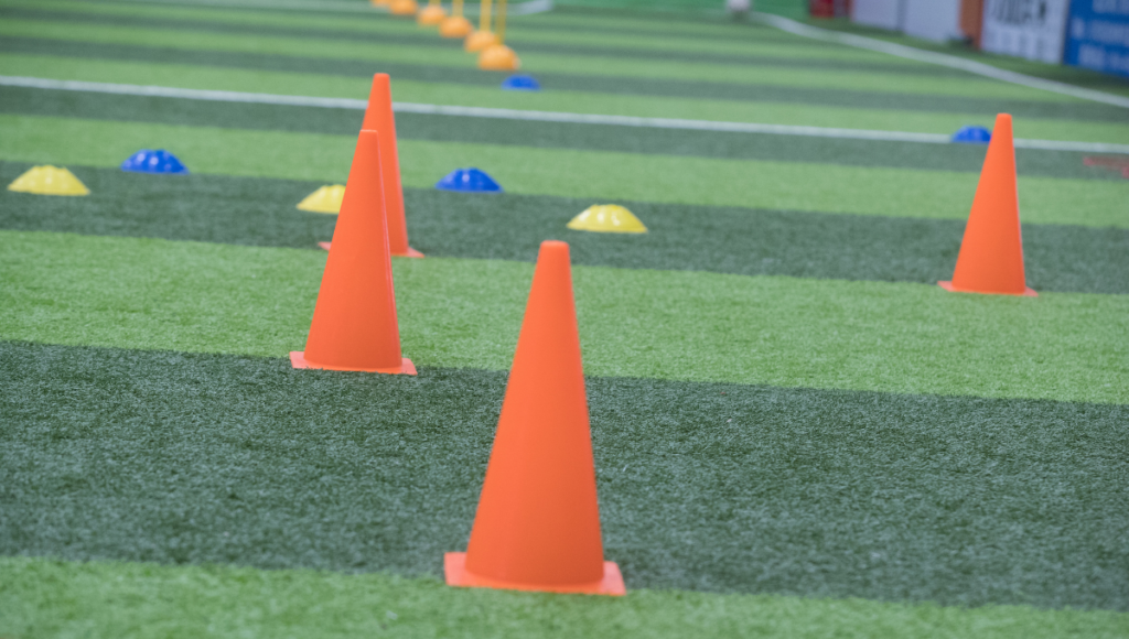 Orange cones arranged on artificial turf with smaller yellow and blue markers in the background, set up for rugby practice.