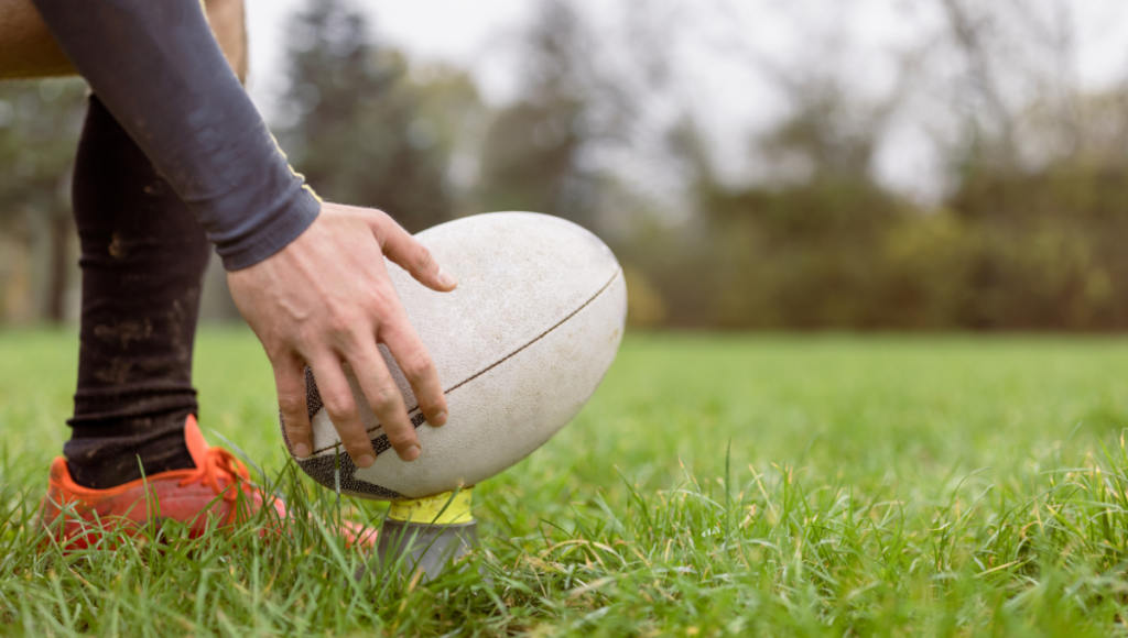 A player positions a rugby ball on a kicking tee, focusing on their setup during a game.