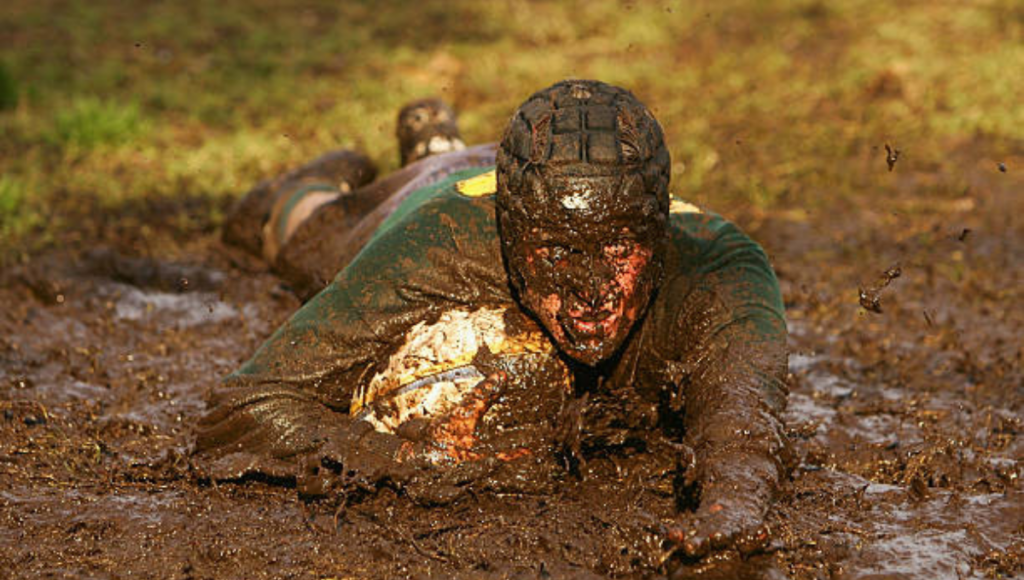 A rugby player fully submerged in the mud, clutching a rugby ball tightly during a match.