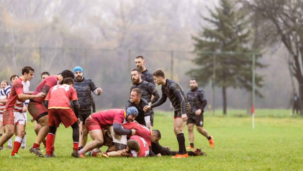 Rugby players engaged in an intense match, showing teamwork and determination in a ruck situation on a wet and muddy field.