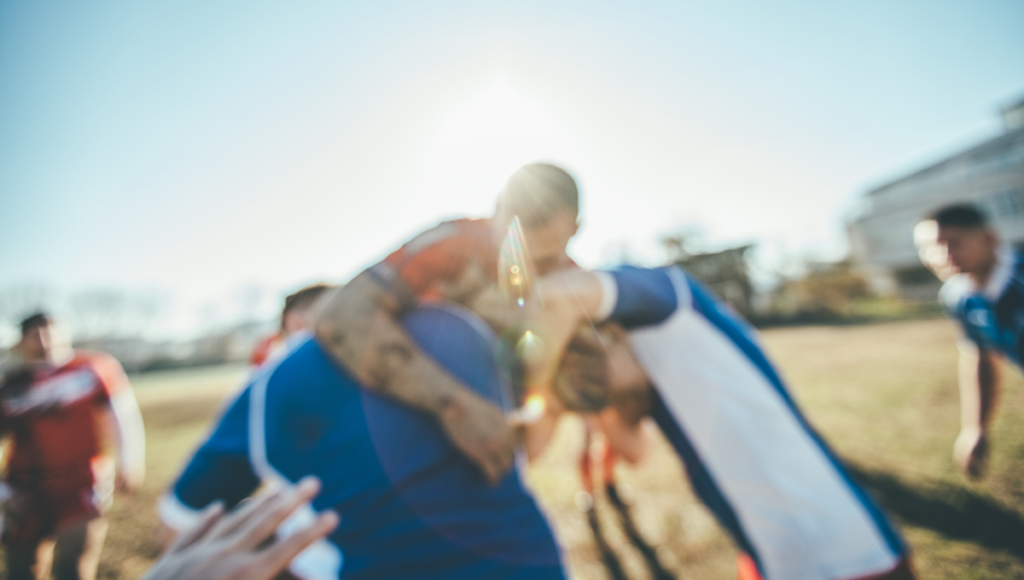 A fierce tackle is captured in motion as players in red and blue jerseys fight for control of the ball, displaying the intensity and physicality of rugby.