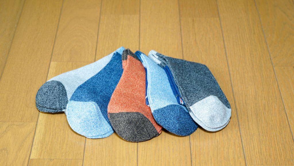 Five pairs of low-cut socks in different shades, neatly laid out on a wooden floor.