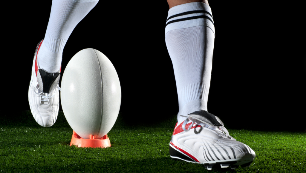 Close-up of a rugby player’s leg and white socks as they prepare to kick a rugby ball on a tee.