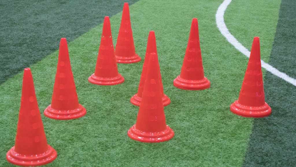 Multiple red training cones arranged in a cluster on artificial turf during a practice session.