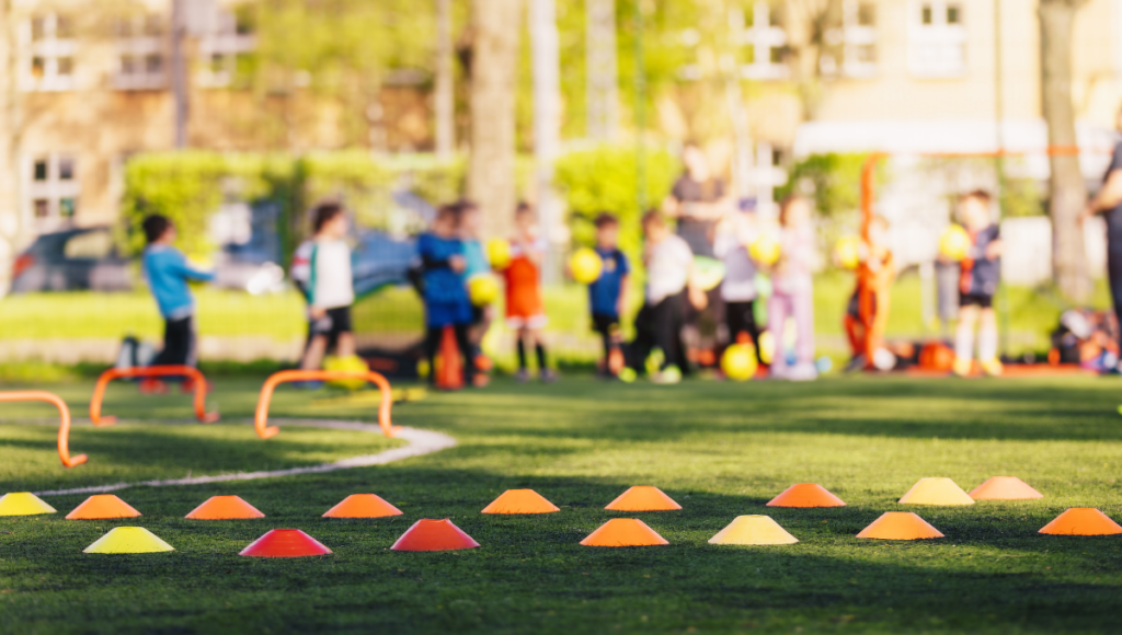 Brightly colored training markers placed on a grass field with children playing rugby in the background during a practice session.