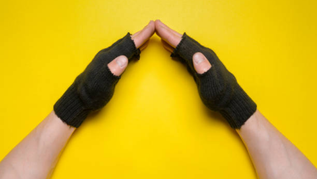 A pair of black knitted fingerless gloves, worn by two hands with fingers touching together, placed against a bright yellow background.