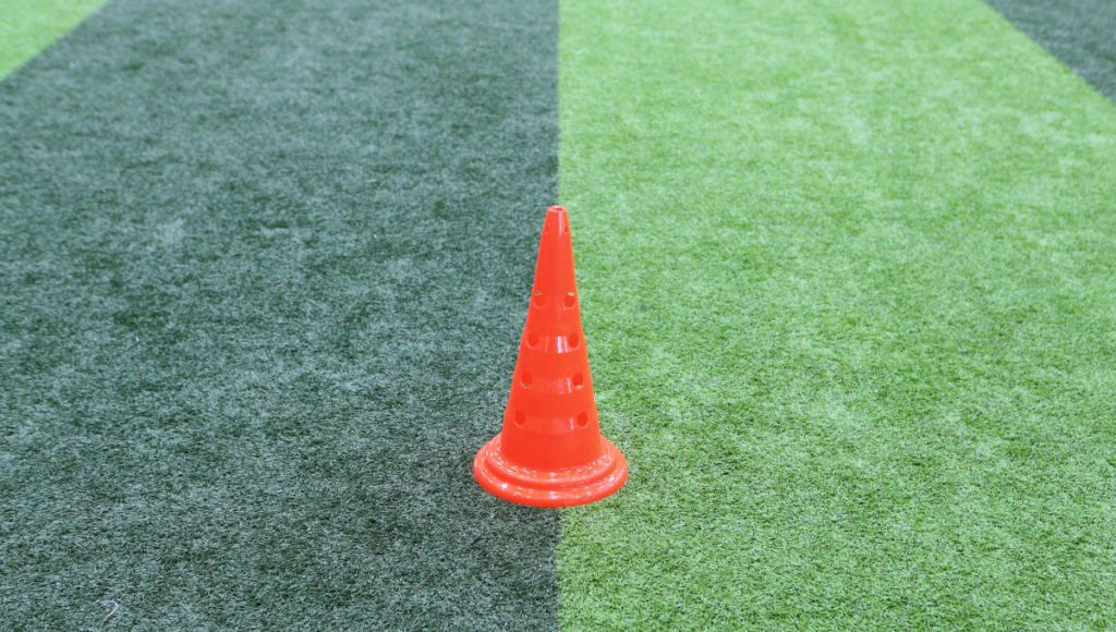 An orange perforated rugby cone standing on artificial turf, ready for use in a training session.