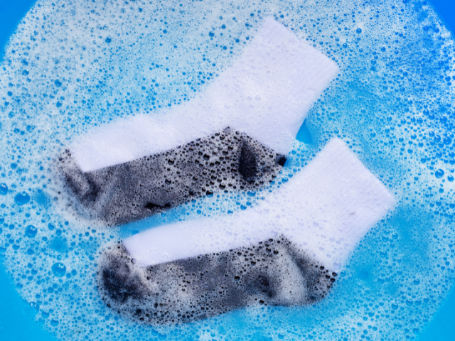 A pair of dirty white socks being soaked in soapy water, showing the cleaning process after use.