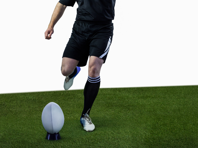 A rugby player prepares to kick a ball placed on a rugby kicking tee on a grassy field.