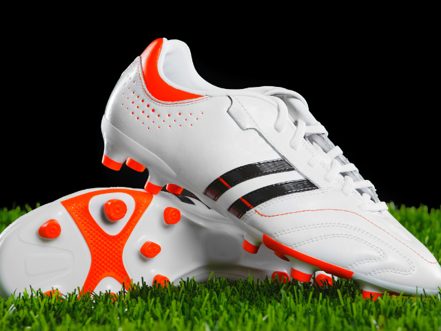 A pair of white and orange rugby boots with clean lines, placed on green artificial turf.