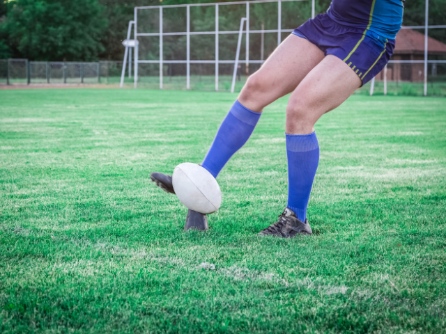 A player preparing to kick an aged rugby ball placed on an orange tee.