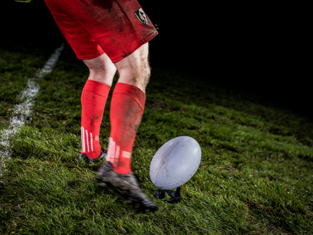 A close-up of a muddy rugby player's foot just about to kick the ball.