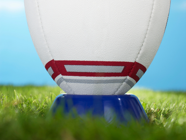 A close-up of a rugby ball placed on a blue kicking tee on a grassy field