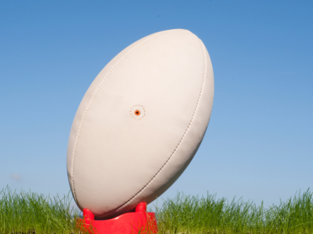 A close-up of a white rugby ball resting on a red tee against a blue sky.

A close-up of a white rugby ball resting on a red tee against a blue sky.