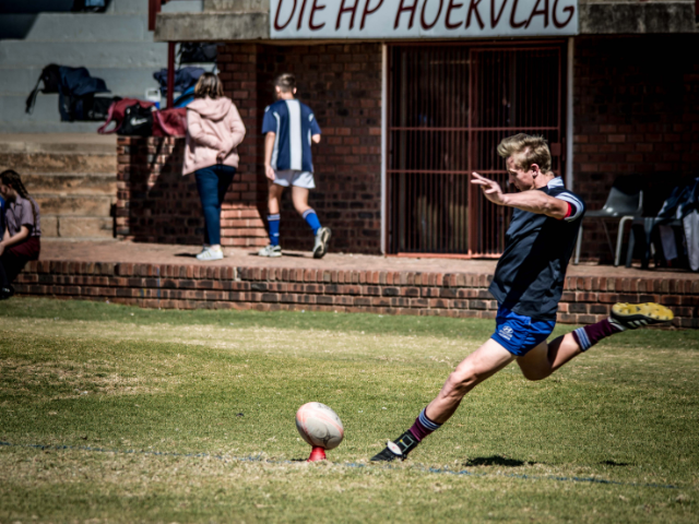 A rugby player in blue socks and shorts kicks the ball during practice.