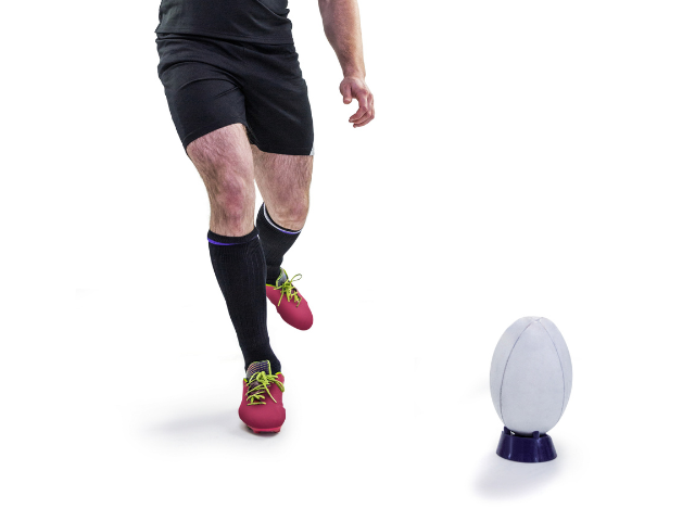 A rugby player prepares to take a kick, focusing on the ball placed on a tee.