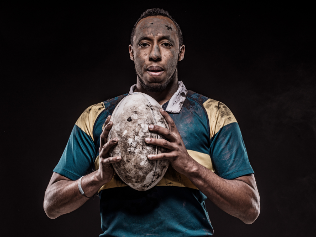 A rugby player covered in dirt holding a rugby ball