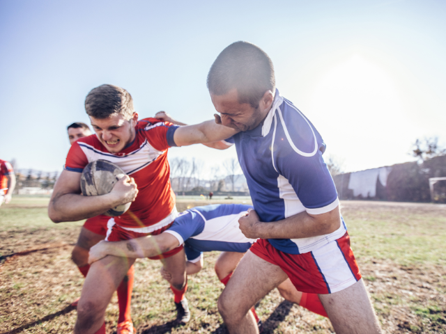 Two rugby players in the middle of a tackle during an intense match, one player holding the ball while the other attempts to push him off.