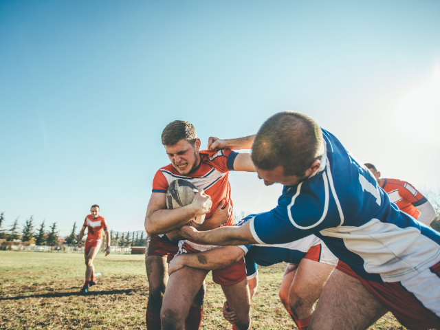 A dynamic and blurred shot of rugby players in a scrum, with the bright sun shining in the background, giving a sense of the fast-paced nature of the game.