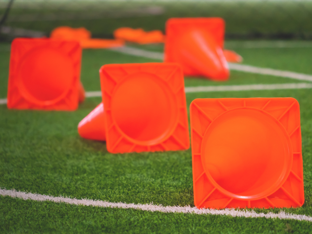 Several orange cones lying on their sides on a grass field, showing the square base design.