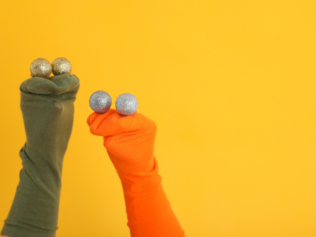 Two colorful sock puppets with glitter balls on their "heads" against a vibrant yellow background.