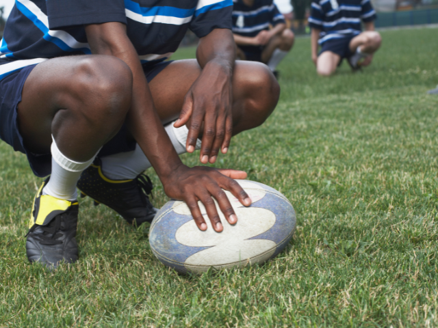 A player preparing to kick off with the ball on the field, wearing black cleats.