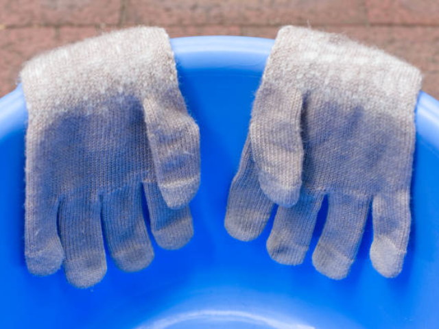 A pair of gray wet gloves drying over a blue plastic bucket.