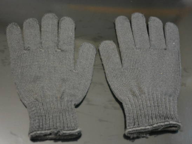 A pair of gray knitted gloves lying flat on a dark surface.