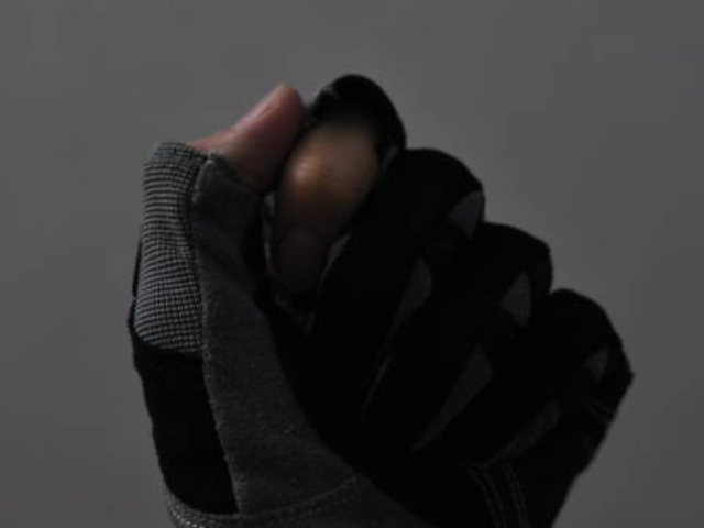 A close-up image of a gloved hand in a half-fist position, the glove is grey with black accents.