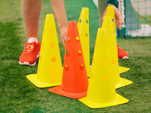 Yellow and orange rugby training cones stacked together on a grass field, with a person setting them up for drills.