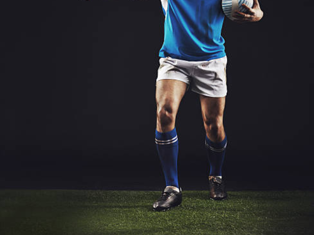 A rugby player in a blue and white uniform, holding a ball and standing on the field.