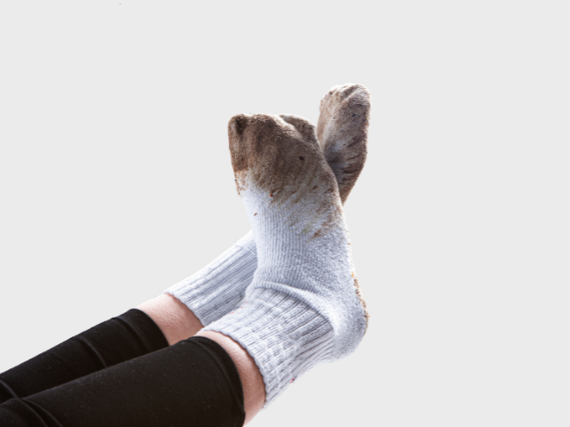 A close-up of dirty white socks on a person's feet, with visible mud and dirt stains.