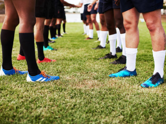 A line of rugby players in different colored cleats and socks standing on the grass, getting ready for a game.