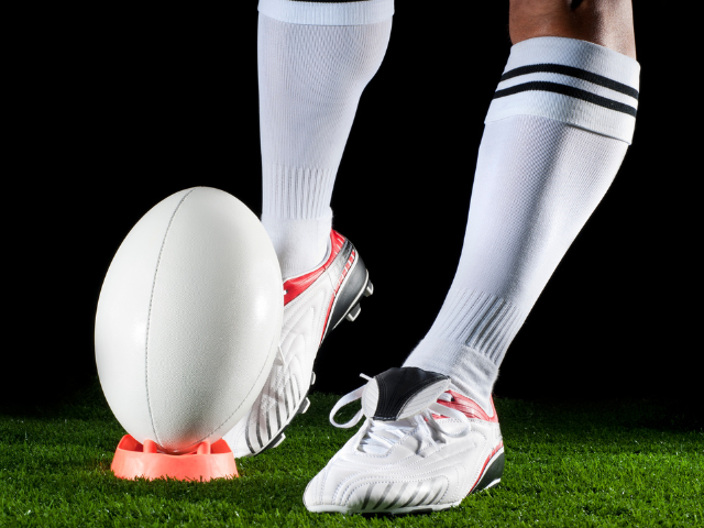 A line of rugby players in different colored cleats and socks standing on the grass, getting ready for a game.