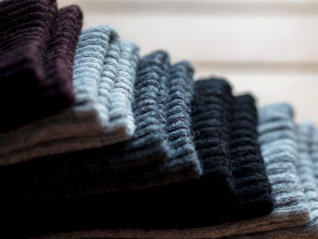 A close-up of folded woolen socks in various shades, including black, gray, and maroon, stacked in a neat pile.