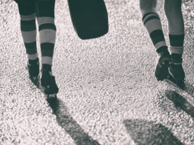 Black and white photo of two rugby players walking side by side, showing only their legs and striped socks.