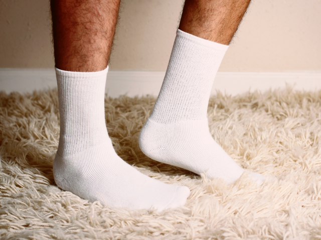 Close-up of a pair of white socks being worn by a person standing on a shaggy carpet.