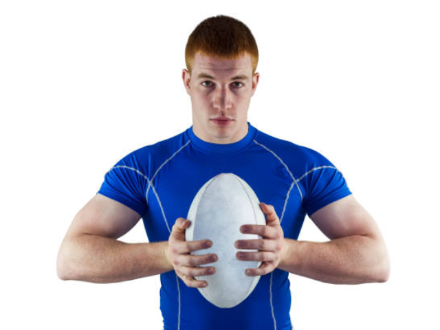 A rugby player holding a rugby ball against his chest, wearing a blue sports shirt, on a white background.