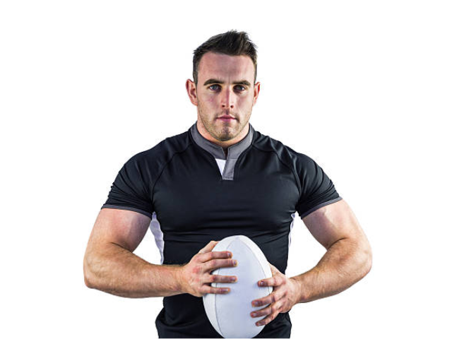 A rugby player in a black shirt holding a white rugby ball, standing in front of a white background, looking serious.