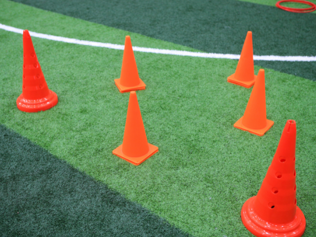 Orange rugby cones of varying sizes arranged in a zigzag pattern on artificial turf.