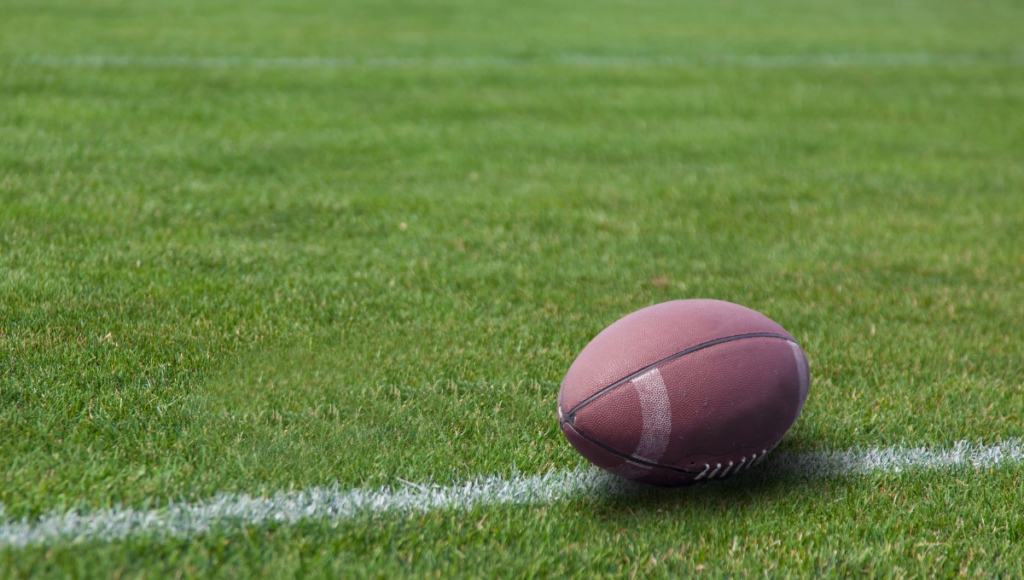 A rugby ball sitting on a well-marked field, near the sideline.