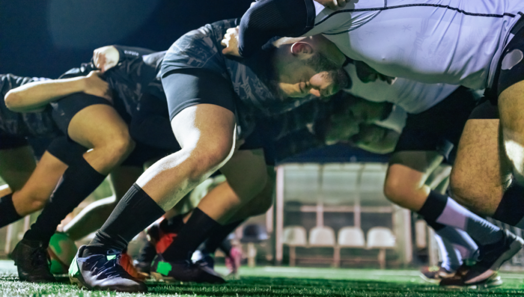 Rugby players in a scrum formation on the field, heads down and ready to engage.