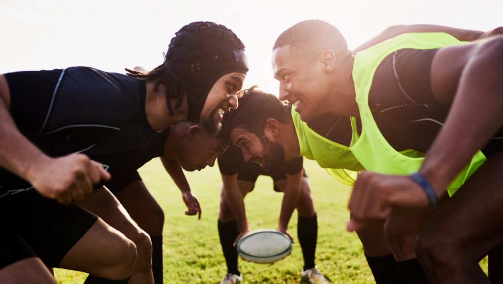 Rugby players wearing black and neon green bibs are locked in a scrum, preparing for a play under the sun.