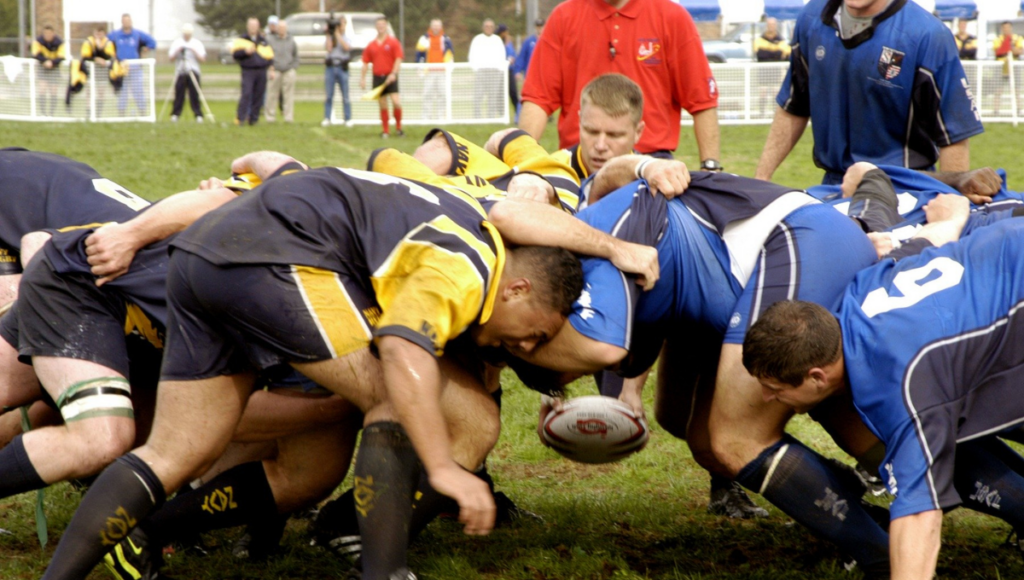 Rugby teams locking heads during a scrum in a muddy field.