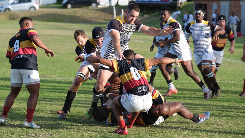 A group of rugby players in colorful jerseys mid-game, tackling and trying to gain possession of the ball.