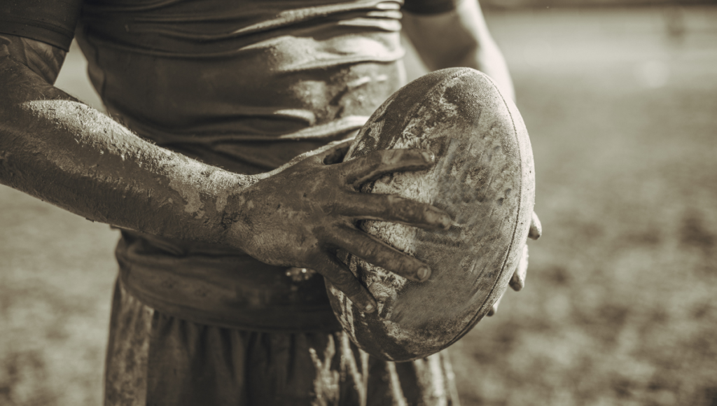 Close-up of a rugby player holding a muddy rugby ball.