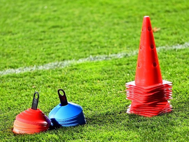 A stack of red and blue flat markers and an orange cone on a green grass field, ready for use in rugby training.