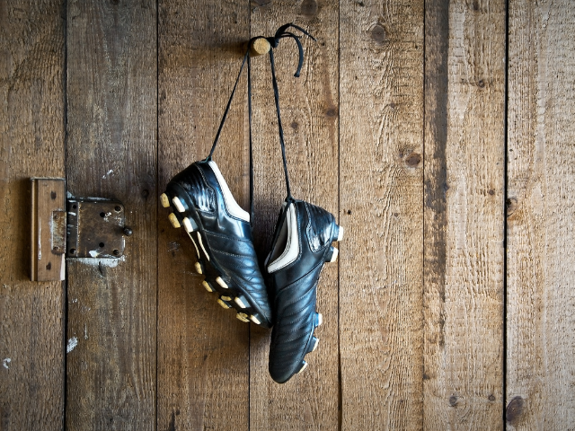 Black rugby boots hanging on a wooden wall.